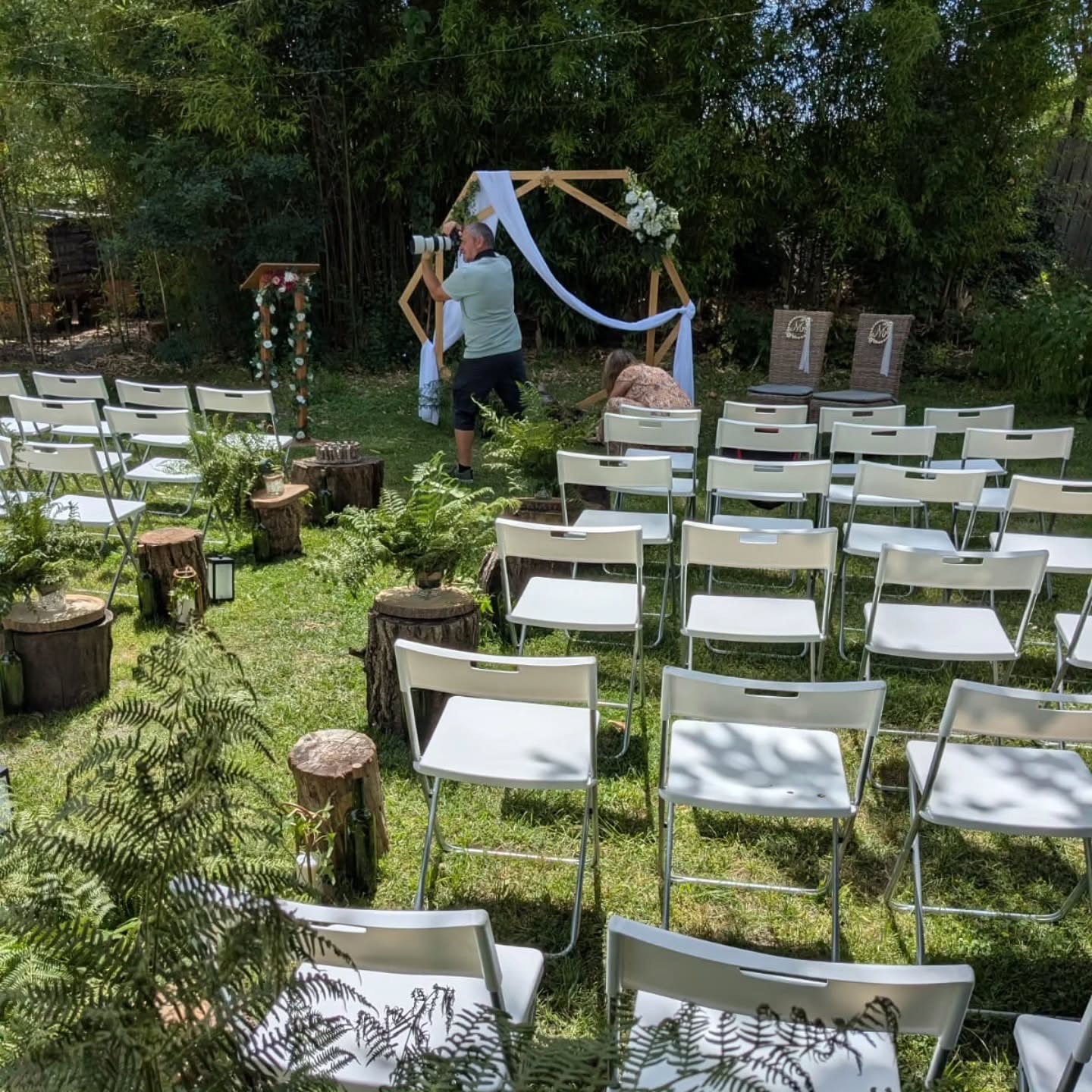 Avant la cérémonie, le photographe au travail et une personne qui ajuste le décor au pied de l'arche en bois